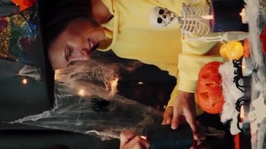 Cadılar Bayramı hazırlıkları. Mutlu arkadaşlar oturma odasında oturuyor, gülümsüyor ve Cadılar Bayramı için mum yakıyorlar. Dikey video. Cadılar Bayramı 'nda oyulmuş balkabağıyla süslenmiş. Mutlu Cadılar Bayramı