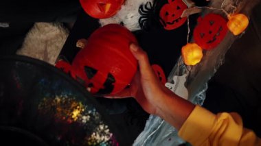Cadı şapkalı bir kadın turuncu balkabağına korkunç bir yüz çiziyor. Jack O Lantern. Cadılar Bayramı gecesini kutluyoruz. Cadılar Bayramı partisi. Dekorasyon ve geleneksel cadılar bayramı sembolü. Dikey video