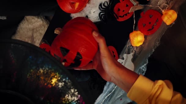 オレンジ色のカボチャの上に怖い顔を描く魔女の帽子の女性 ジャック オランタン ハロウィーンの夜を祝う ハロウィンパーティー 装飾と伝統的なハロウィーンのシンボル バーティカルビデオ — ストック動画