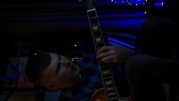 年轻英俊的吉他手一个人弹奏吉他 音乐家穿着蓝色衬衫弹奏电吉他 音乐产业的概念 音乐家在黑暗的房间里用吉他演唱歌曲 垂直录像 — 图库视频影像