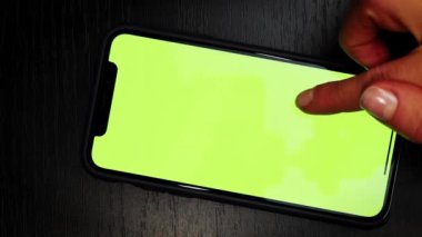 Elinde yeşil ekran olan telefon. Kromakey ekran kopyalama alanı. Masa arkasında yeşil ekranlı akıllı telefonu tutan, kaydıran ve kaydıran kişinin elleri. Dikey video