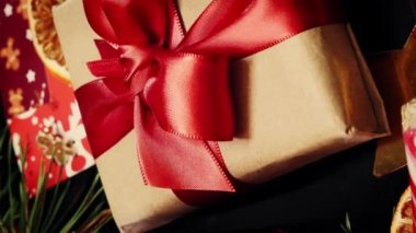 Kırmızı kurdeleli Noel hediyesi kutusu süs ve dekorasyonlu Noel arkaplanına karşı. Noel selamları. Yeni yıl hediyeleri, şenlik ve tatil süslemeleri. Tatil hediyesi. Dikey video