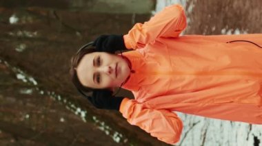 Kadın ormanda koşar. Kış parkında koşan turuncu ceketli genç bir kadın. Formda bir sporcu sabahları sıkı antrenman yapar. Park 'ta yoğun bir kadın eğitimi. Dikey video