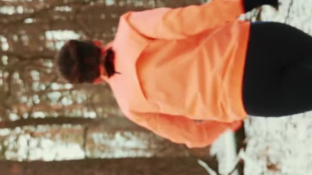 女人在森林里跑年轻自信的女性穿着运动服在冬季森林的灌木丛中慢跑 女人跑开 后边跟着视线 在室外跑步 垂直录像 — 图库视频影像