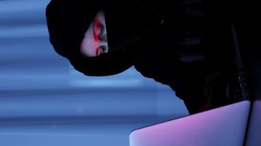 Hacker bilgisayardaki çevrimiçi güvenlik korumasını kırıyor. Siyah maskeli bir kadın, kapüşonlu kodlama ve dizüstü bilgisayar programlama. Bilgisayar korsanı klavyede yazıyor. Çevrimiçi, web geliştirme. Dikey video