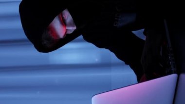Kendine güvenen erkek hacker dizüstü bilgisayar ekranına bakıyor. Siyah maskeli ve kapüşonlu bir adam karanlık odada oturuyor ve online sosyal güvenlik korumasını hackliyor. Bilgisayar şifresini kıran genç bir hacker. Dikey video
