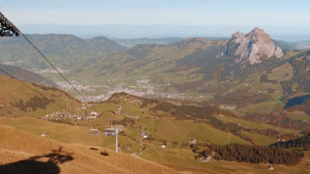 スイスの山のスキーリフトは 上下に持ち上げる人々と カラフルな木々と丘のある秋の風景 スイスの山でスキーリフトに乗る旅行者 アウトドア活動 — ストック動画