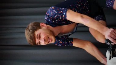 Bisikletçi evde spor yapıyor. Spor salonundaki akıllı antrenörlere biniyor ve yüzünü havluyla siliyor. Sabit bisikletli erkek sporcu eğitimi. Fitness spor antrenmanı. Kapalı alanda bisiklet sürmek. Dikey video