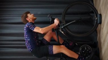 Profesyonel bisikletçi bisiklet aralığı egzersizlerini akıllı eğitmenle yapıyor. Adam sabit bisiklet eğitmeninde pedal çeviriyor. Ev içi bisiklet konsepti. Çevrimiçi fitness çalışması. Spor motivasyonu. Dikey video