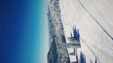 Kayak merkezi Feldberg, Schwarzwald, Almanya, güneşli kış gününde. Dikey video. Kayak merkezinde kayak pistleri ve kayak asansörleri. Aktif insanlar kışın yamaçlarda ve tepelerde kayak ve snowboard yapıyor. Kış sporu