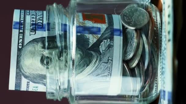 人们把装有美圆钞票的玻璃瓶放在里面 100美元钞票在玻璃钱箱 旋转镜头 节约资金的概念 财务概念 垂直录像 — 图库视频影像