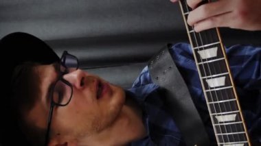 Gitarda çalan bir genç. Elektro gitarla çalan komik stil müzisyeni. Mutlu gülümseyen gitarist elektro gitar çalıyor, yeni akorlar çalışıyor. Gitar dersleri. Dikey video