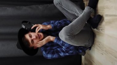 Kulaklıkla müzik dinleyen bir adam. Şapkalı ve tişörtlü genç kız evde oturmuş müzik dinliyor ve şarkı söylüyor. Müzik konsepti. Dikey video