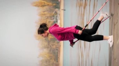 Kuzeyli yürüyüşü. Sabahleyin yarışma ve maraton için İskandinav yürüyüş direkleri antrenmanı yapan tombul bir kadın. Sağlık konsepti. Geniş vücutlu, açık havada egzersiz yapan genç bir bayan. Dikey video