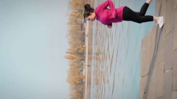 若い女性は マラソンのトレーニング中に工業都市川に沿って簡単なジョギングをするように動機づけました 屋外で走り 激しい心臓トレーニングを行い 体重を減らそうとしています バーティカルビデオ — ストック動画