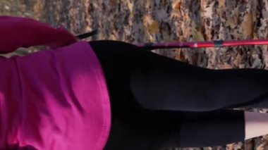 Tombul kadın, kilo verme programının bir parçası olarak sonbahar parkında İskandinav yürüyüş programı yapıyor. Geniş vücutlu genç bir kadın dışarıda egzersiz yapıyor, spor yapıyor. Dikey video