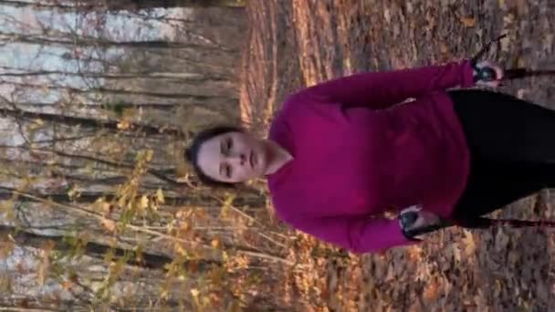 ノルディックウォーキングコンセプト 秋の森や公園でノルディックウォーキングポールのトレーニングを持つチャビー女性 減量コンセプト 若者は屋外で運動する大きな体重を持つ女性を動機づけました バーティカルビデオ — ストック動画