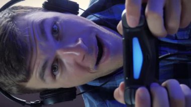 Kablosuz joystick ile online video oyunu oynayan erkek oyuncunun portresi. Kulaklıklı adam konsolda oyun oynuyor. Dikey video