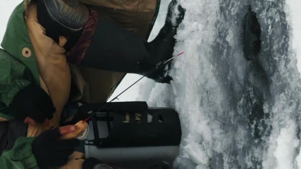 フィッシングロッドの閉鎖 アイスホールで魚を捕まえる漁師 凍った川や湖で釣る男 冬の釣り バーティカルビデオ — ストック動画