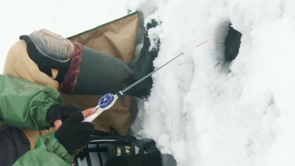釣り棒を持つ男は 氷穴で魚を捕まえています 漁師は凍った湖で釣りをしている 冬の釣り バーティカルビデオ — ストック動画