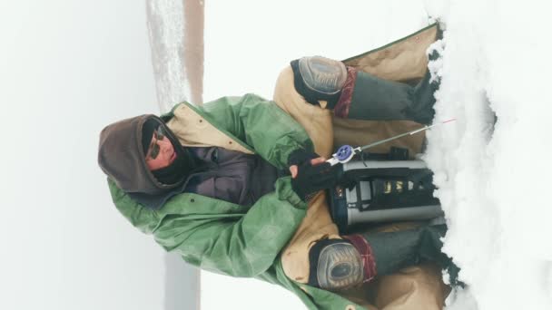 冬の釣り アイスホールで釣り棒で釣りをする漁師 凍った湖で釣る男 冬の極端な漁具について バーティカルビデオ — ストック動画