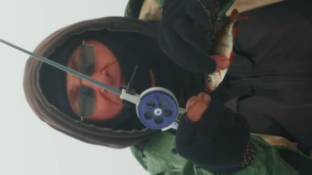 漁師は氷の穴で魚を捕まえました 冬に凍った湖で魚を釣った バーティカルビデオ — ストック動画