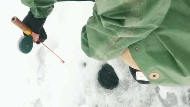 用钓竿把冰洞关上 渔夫正在结冰的湖上钓鱼 人在冬天捕鱼 垂直录像 — 图库视频影像