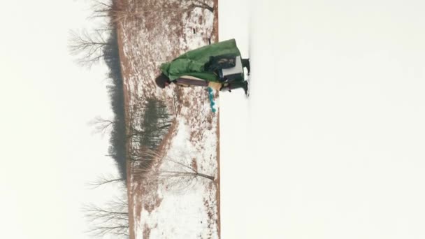 漁具と氷ドリルを積んだ漁師が凍った湖を通り抜けている 冬の極端な寒い服を着ている男性は 冬に凍った川を歩いています バーティカルビデオ — ストック動画