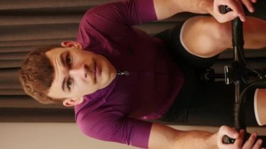 Adam evde bisiklet eğitmeni olarak çalışıyor. Bisikletçi, kapalı alanda sabit bisiklet üzerinde sıkı çaba gösteriyor. Dikey video