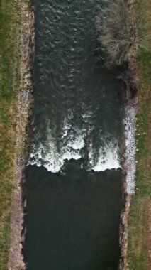 Nehir akıntısı şeffaf suyla, dikey videoyla akıyor. Taşların arasından hızla akan suyun en üst drone görüntüsü. Doğa arkaplanı