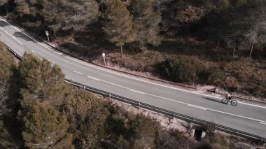 Bisikletçinin dağlarda bisiklet sürüşünü gösteren hava manzarası. İspanya 'da boş yolda bisiklet süren kadın sporcu, sıkı çalışma. Kasklı ve bisiklet ayakkabılı bir kadın bisiklet üstünde tepeye doğru pedal çeviriyor.