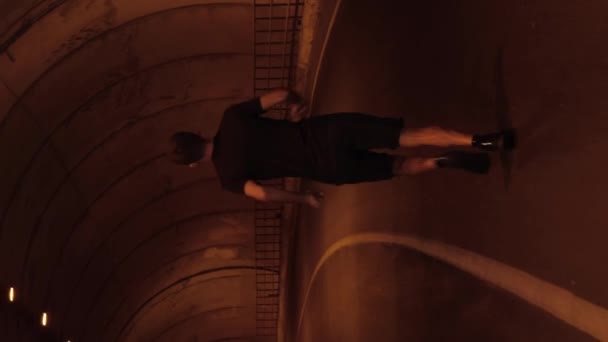 高山地帯の空のトンネルを走る男性選手 車のトンネルでジョギングする黒いスポーツ服の男 バーティカルビデオ — ストック動画