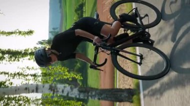 Bisiklet giysisi ve kask takan sportif formda bir kadın bisiklet sürerek kırsal alanda tepeye çıkıyor. Dikey video. Dağlarda bisiklet süren şık bir bisikletçi.