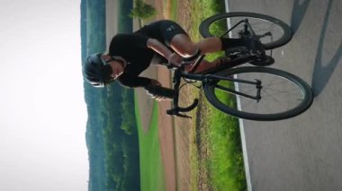 Bisikletçi bisiklet sürerken su içiyor. Dikey video. Kadın sporcu bisiklet sürerken biberondan izotonik içer. Yol bisikleti ve triatlon