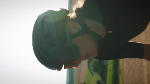 穿着时髦自行车 骑自行车 头戴金色夕阳灯的活泼女人的画像 垂直录像 夏季日落时 骑单车上山的专业骑单车者 — 图库视频影像