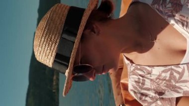 Hasır şapkalı ve güneş gözlüklü bir kadın göl boyunca teknede yüzüyor. Güneşli yaz gününde dişi, elektrikli teknede yüzer. Dikey video