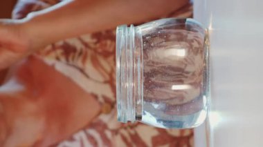 Yaşlı kadın bir bardak suya takma diş koyuyor. Takma dişler bir bardak suya düşüyor. El, takma dişleri cama yerleştirir. Dikey video