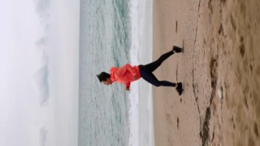 Fırtınalı havada kıyı şeridi boyunca koşan bir kadın. Spor giyimli tombul kadın deniz kıyısında koşuyor. Spor konsepti. Dikey video