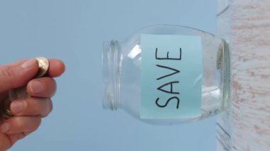 Cam kavanoza yapışkan bir notla bozuk para koy. Kaydet. Kadın para biriktirmek için kavanoza para koyuyor. Finansal konsept. Dikey video