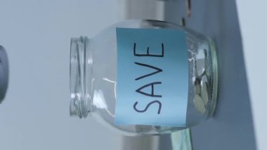 Dolarları bozuk paralarla dolu kavanoza koymak. Tasarruf kavanozunda. Biriktirilmiş para ile şeffaf kavanoza para koyan kişi. Dikey video