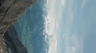 Pilatus Dağı 'ndan İsviçre Alplerindeki karlı kayalık dağların manzarası. Dikey video. İsviçre 'de kar ve sisle kaplı dağların üzerinden uçan helikopter.