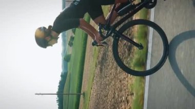Yol bisikleti. Güneşli yaz gününde bisiklete binen bisikletçi. Siyah stil spor kıyafetleri giymiş bir kadın yol bisikletinde antrenman yapıyor. Dikey video