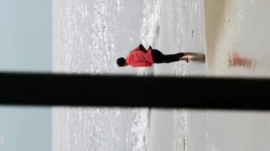 Genç kadın büyük dalgalarla fırtınalı denizde tek başına yürüyor. Mavi dalgalı ve beyaz köpüklü güzel deniz ve okyanus manzarası. Dikey video