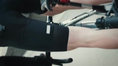 Formda kaslı erkek bacakları bisiklet yolunda pedalları itiyor. Bisikletli sporcu antrenmanı, yakın çekimde bisiklet. Dikey video