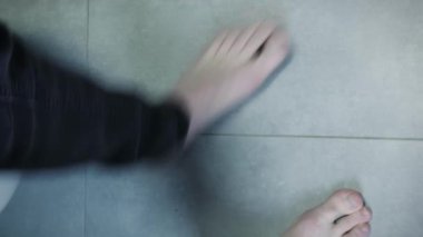 Adam tuvalette oturuyor. Kotlu ve iç çamaşırlı çıplak ayaklı bir erkek banyodaki gri fayanslı beyaz tuvalete oturuyor. Ayaklar banyoda tuvalete oturur. Dikey video