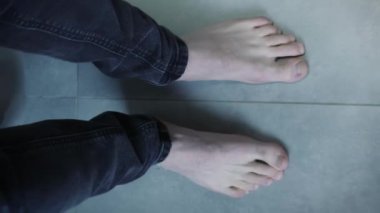 Gri banyodaki tuvalette çıplak ayaklı erkek bacaklarının üst görüntüsü. Dikey video