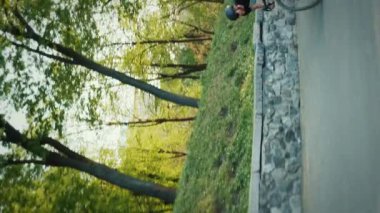 Güçlü bir atletik bisikletçi eyerden yukarı doğru koşuyor. Bisiklet sürücüsü yeşil tepeye tırmanıyor siyah spor giyim ve miğfer giyiyor. Dikey video