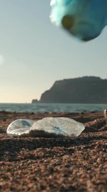 Female hands in protective blue gloves collecting plastic garbage on beach. Volunteer cleaning beach from plastic bottles and trash, collecting trash in trash bag. Vertical video