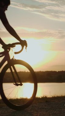 Günbatımında kadın bisikletçi. Günbatımı ışıklarında gölün önünde duran bisikletli profesyonel bir bisikletçi. Dikey video