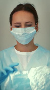 Portrait of young female scientist in doctor uniform and protective face mask puts on medical cap. Woman face in medical mask and cap for virus infection prevention and protection. Vertical video